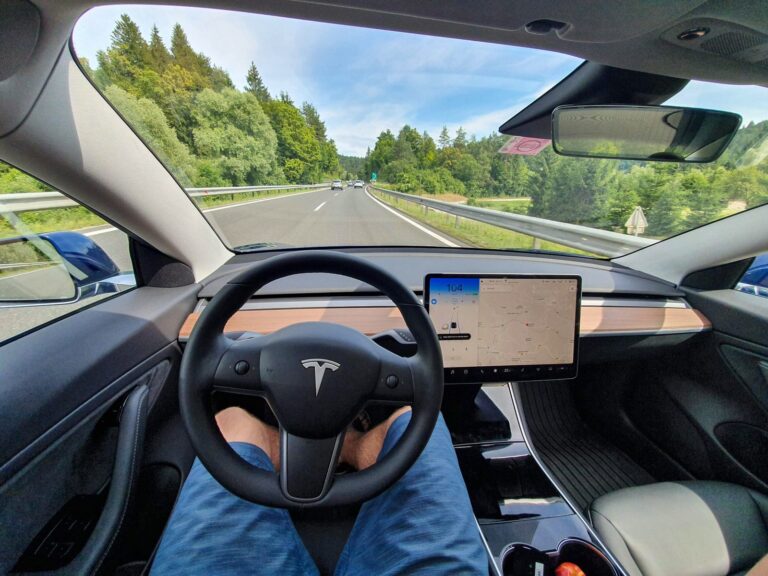 Driving down an empty highway in a high-tech autonomous Tesla vehicle. Young man drives along a scenic rural motorway hands-free in a modern self-steering car.
