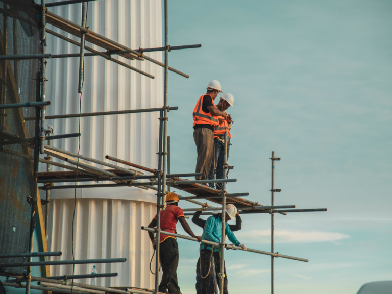 A construction crew in hard hats and safety vests standing on scaffolding.