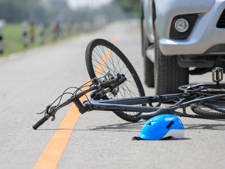A bicycle in the road with a helmet under a car.