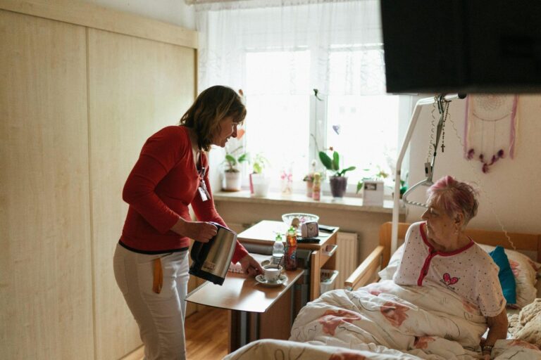 A woman in a nursing home bed with a staff member.